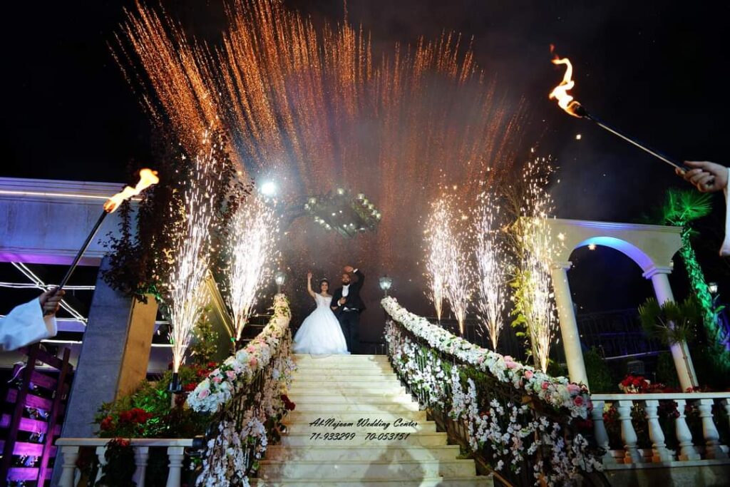 a couple in wedding attire on stairs with fireworks in the background