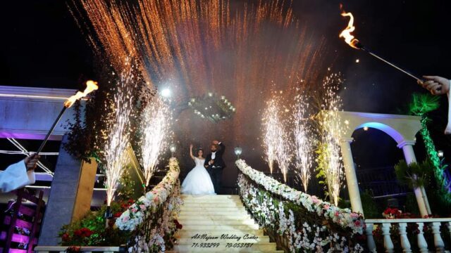 a couple in wedding attire on stairs with fireworks in the background