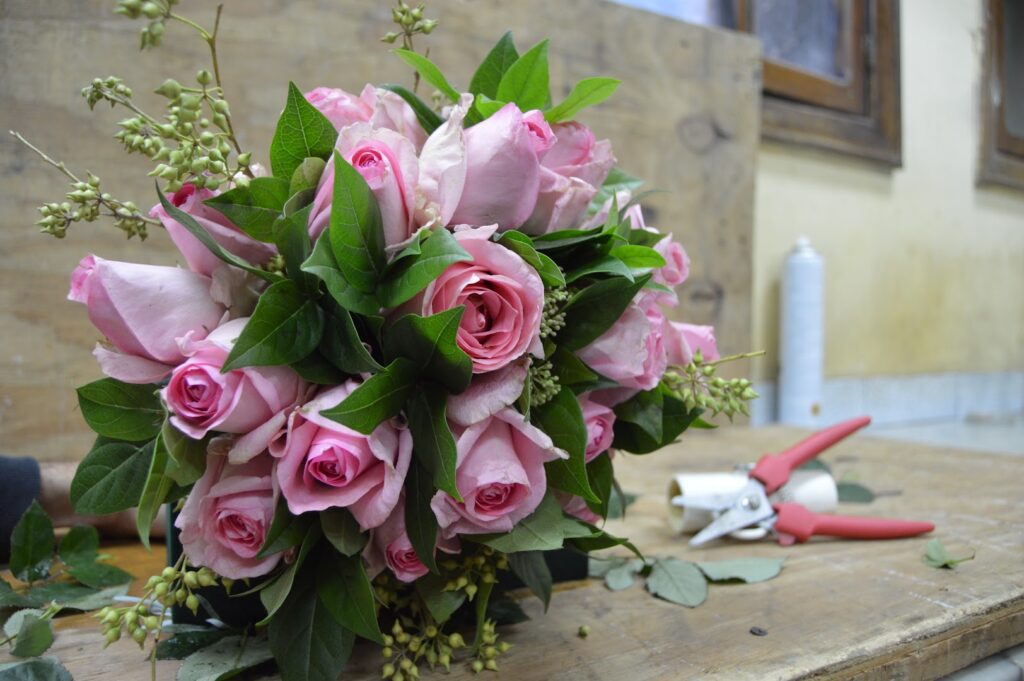 a bouquet of pink roses and scissors on a wood surface
