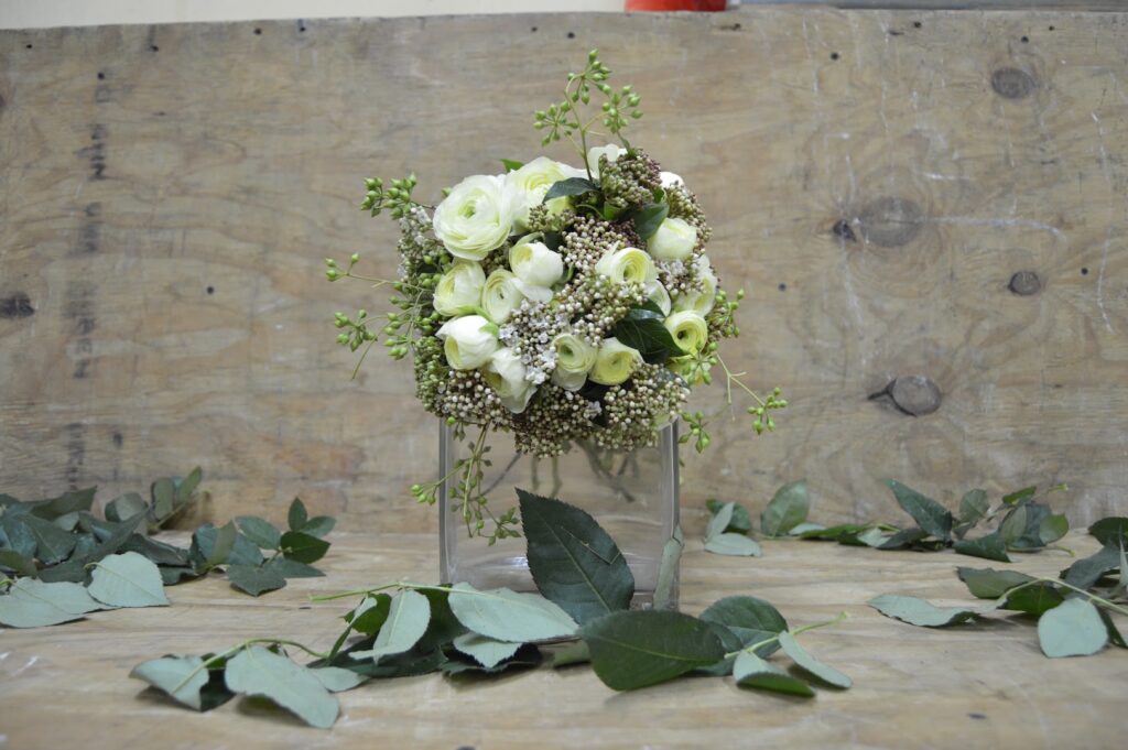 a bouquet of white roses and green leaves in a glass vase