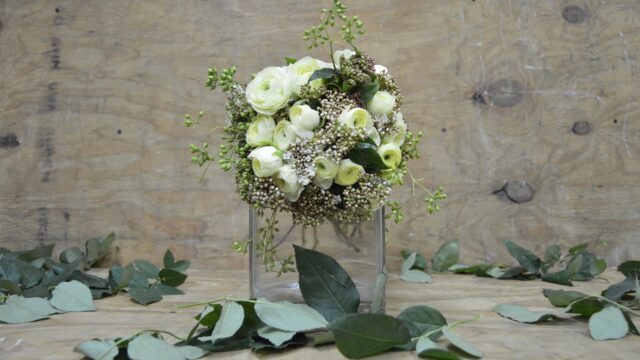 a bouquet of white roses and green leaves in a glass vase