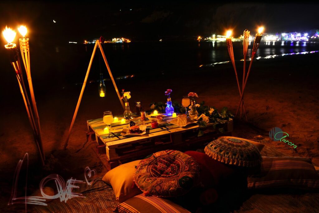 a table with candles and pillows on a beach at night