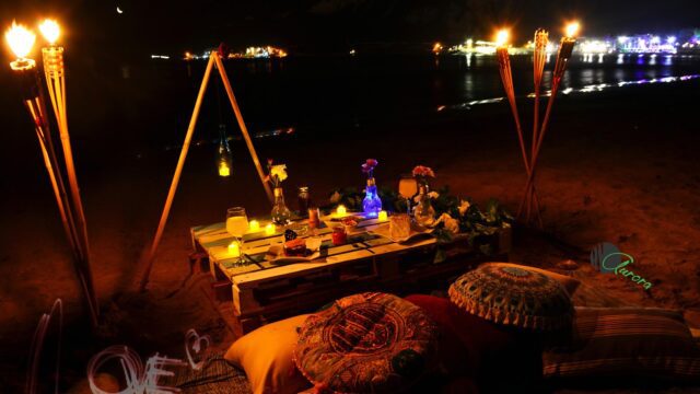 a table with candles and pillows on a beach at night