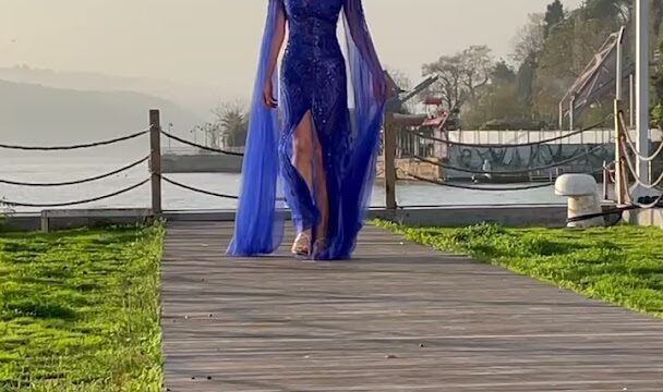 a woman in a blue dress walking on a wooden walkway