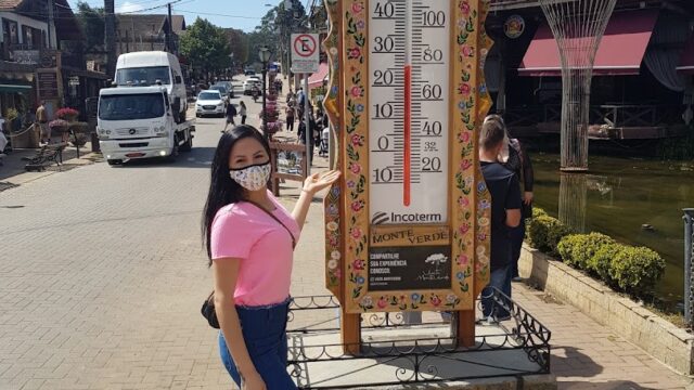 a woman wearing a face mask standing next to a thermometer