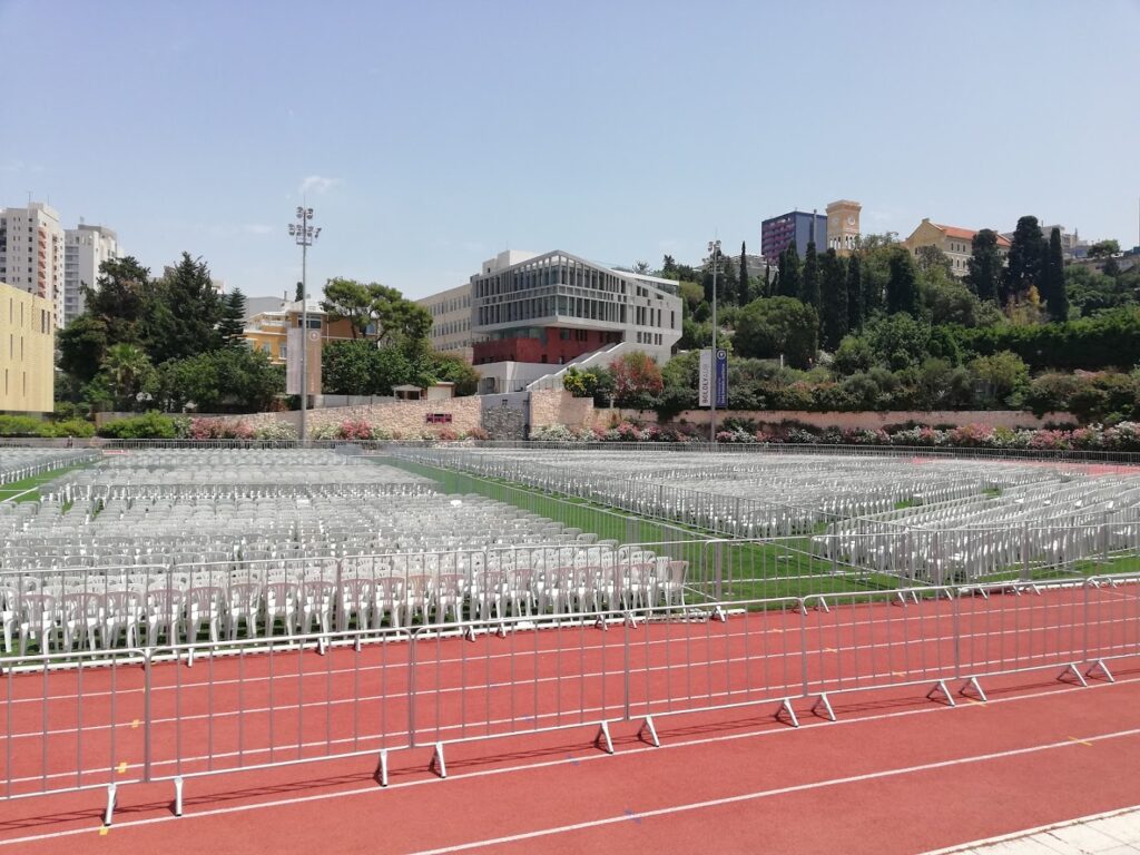 A stadium with rows of Beydoun Chairs كراسي بيضون, white seats, and a red track.