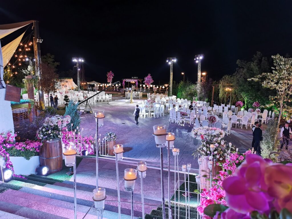 a group of people walking in a courtyard with white chairs and flowers