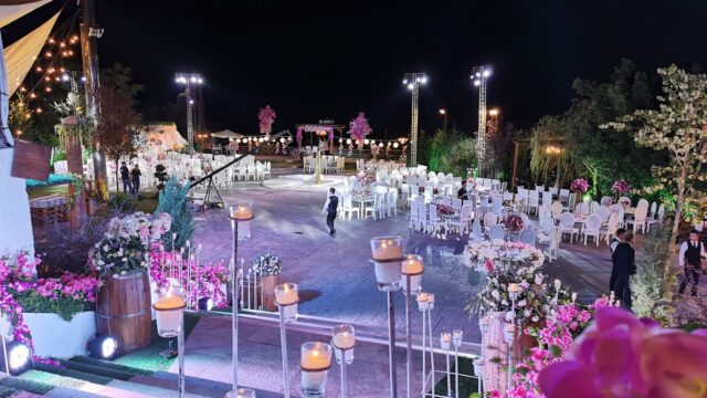 a group of people walking in a courtyard with white chairs and flowers