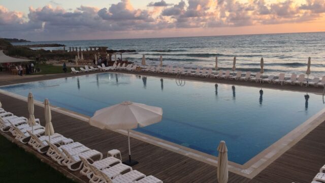 a pool with chairs and umbrellas by the ocean