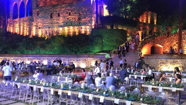 a group of people sitting at tables in front of a stone building