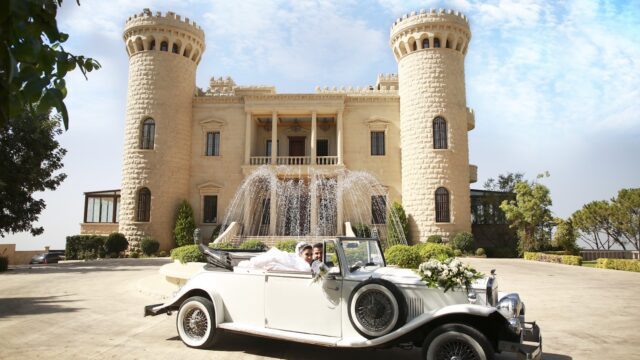 a man and woman in a car with a fountain in front of a castle