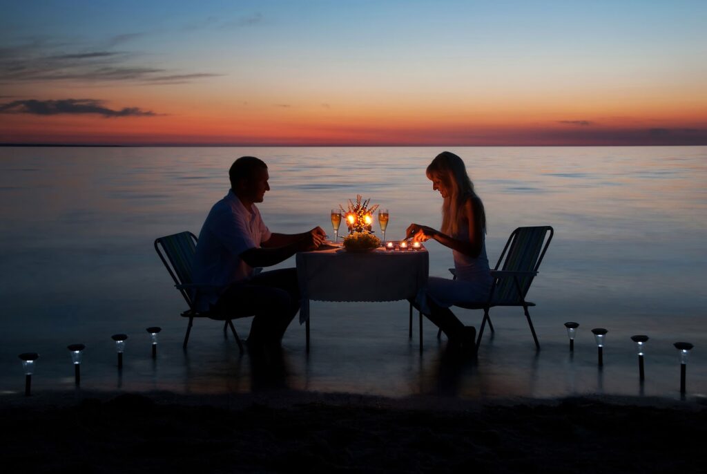 a man and woman sitting at a table with candles on the water