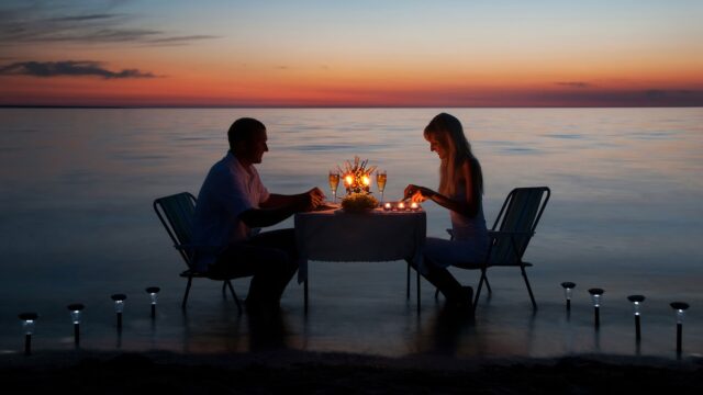 a man and woman sitting at a table with candles on the water