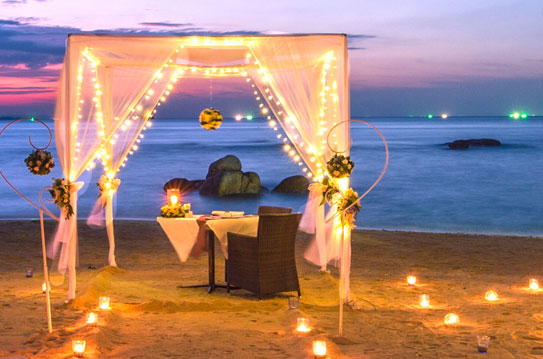 a table set up on a beach with candles and lights