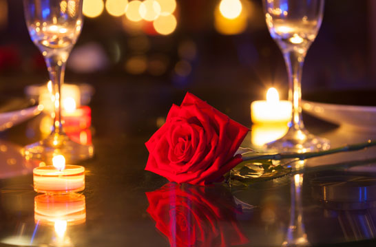 a rose on a table with candles and wine glasses