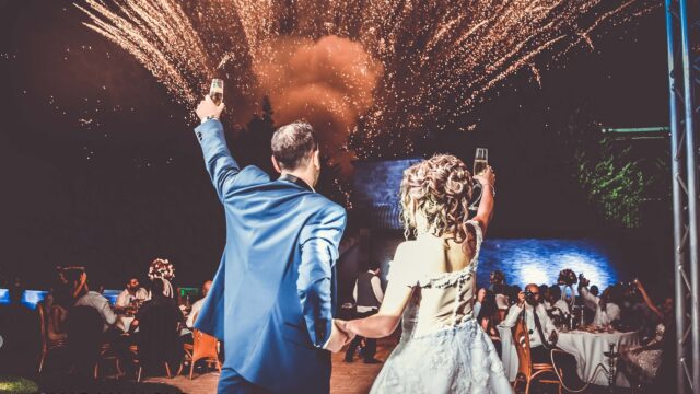 a man and woman holding hands and dancing with fireworks in the background