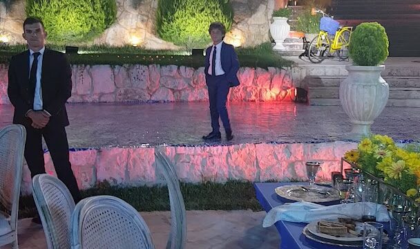 a man in a suit standing on a stage with a table and chairs