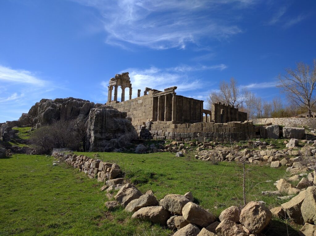 a stone building with columns and rocks in a grassy area