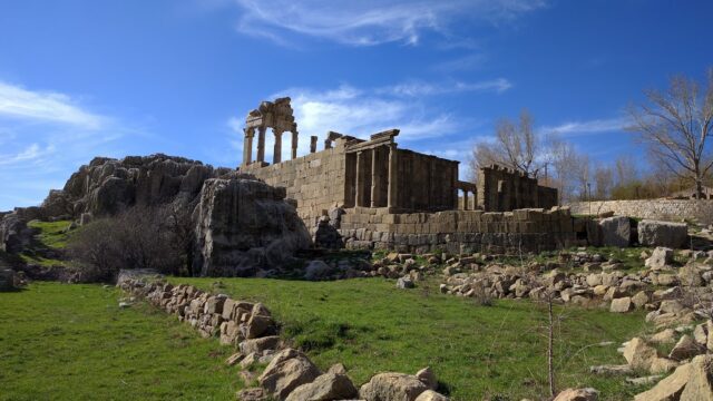 a stone building with columns and rocks in a grassy area