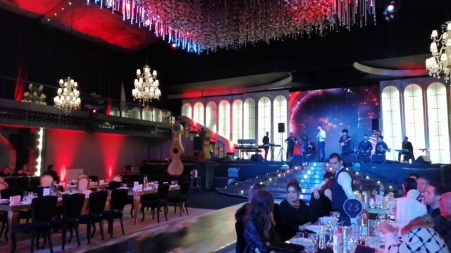 a group of people sitting at tables in a room with a stage and a stage with a chandelier and a stage with a band playing on it