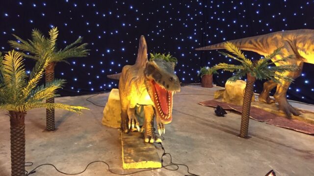 a dinosaur model in a room with palm trees and lights