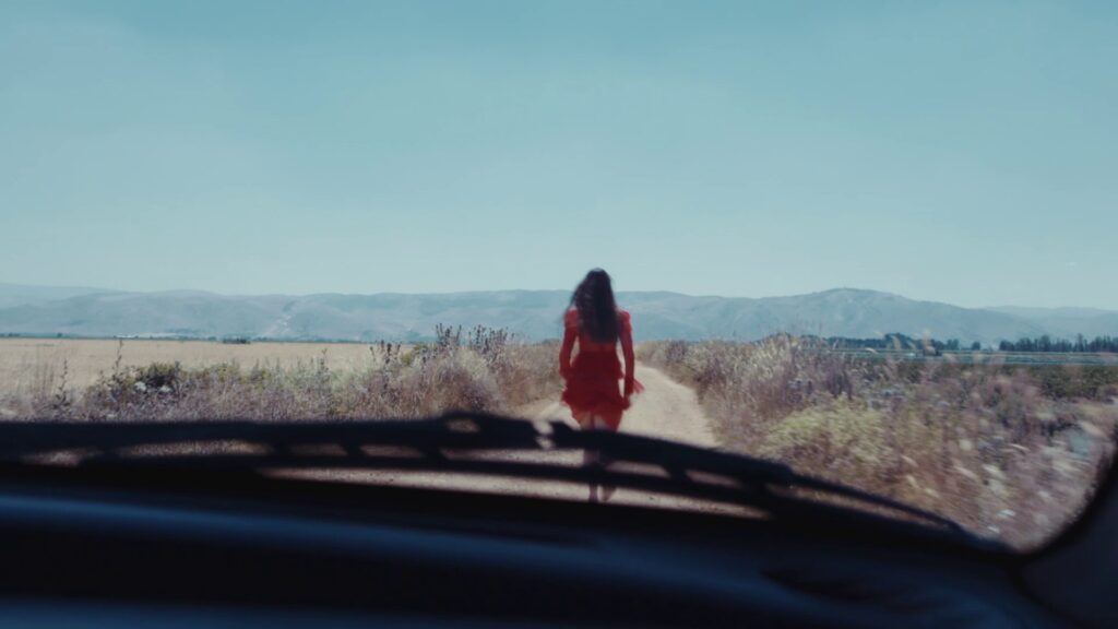 a woman in a red dress walking on a dirt road