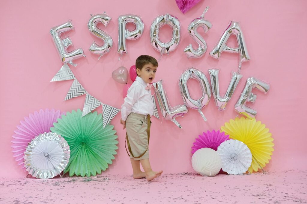 a boy standing in front of a pink wall with balloons