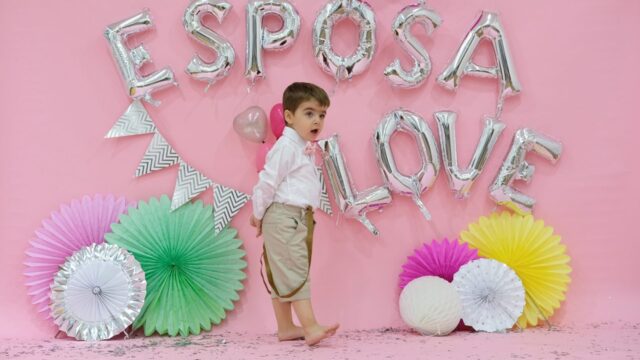 a boy standing in front of a pink wall with balloons