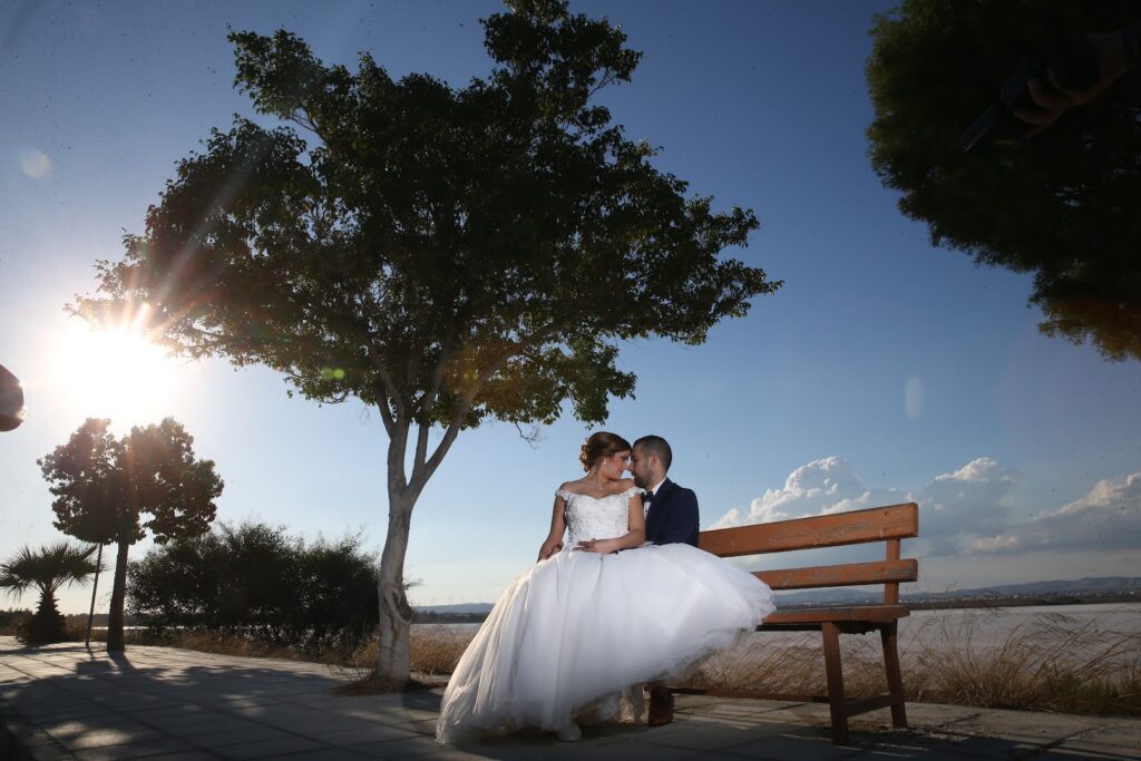 a man and woman in wedding dress sitting on a bench under a tree