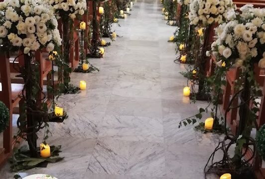 a church aisle with white flowers and candles