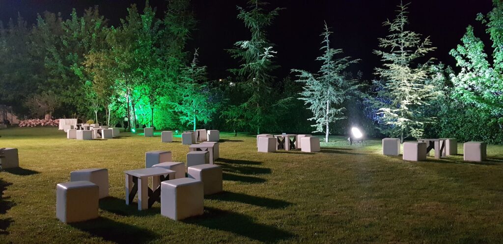 a group of white tables and benches in a grassy area with trees and lights