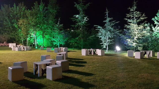 a group of white tables and benches in a grassy area with trees and lights