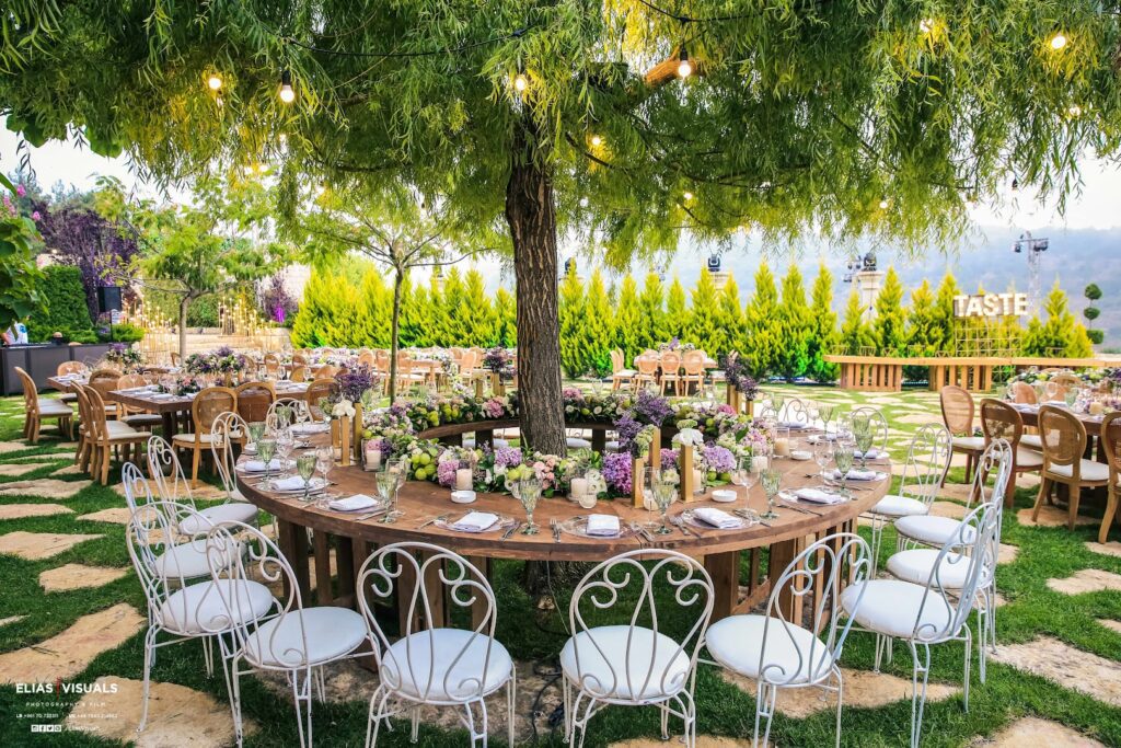 a table set up under a tree with white chairs