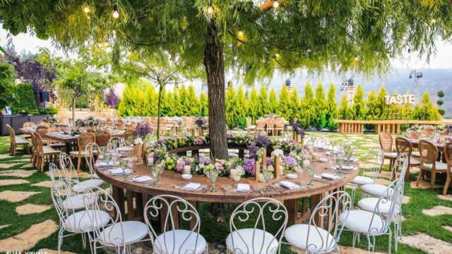a table set up under a tree with white chairs