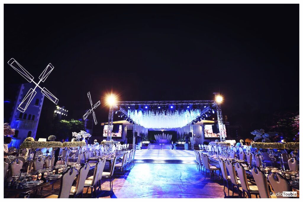 A stage with tables and chairs, lights, and Al Tawahin .