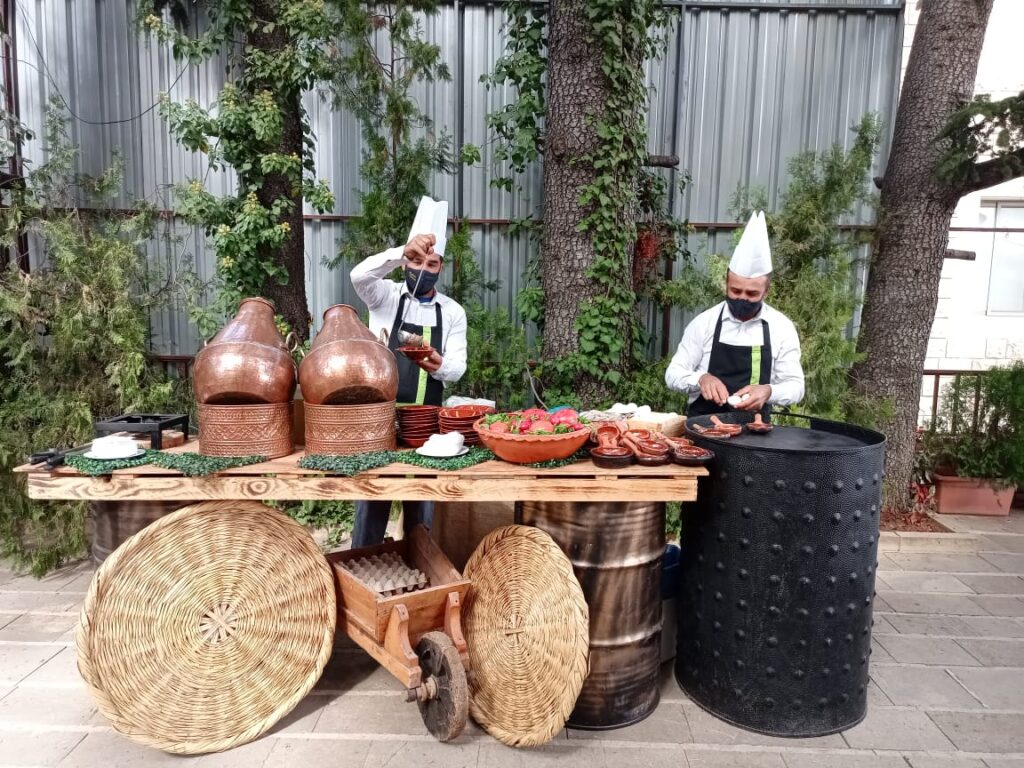Two men from Baskinta Catering are cooking outside in front of a table full of food.