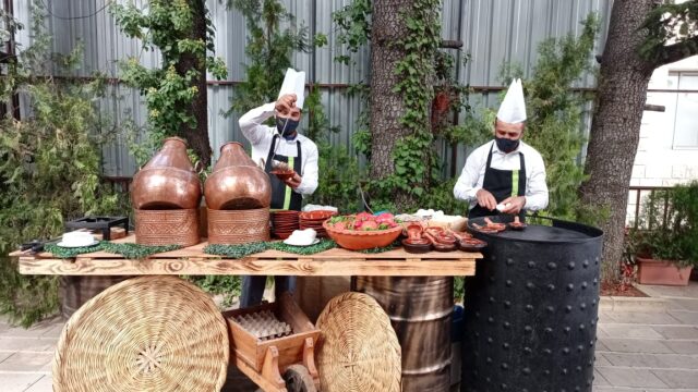 Two men from Baskinta Catering are cooking outside in front of a table full of food.