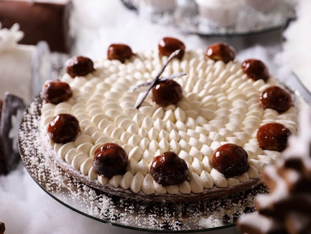 Bluemz Catering presents a cake with white frosting and brown balls on top.