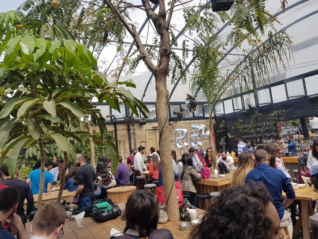 a group of people sitting at tables in a room with trees and plants