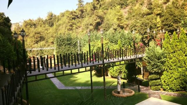 a bridge over a lawn with trees and a statue