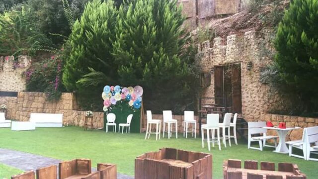 a lawn with chairs and tables and a wall with trees