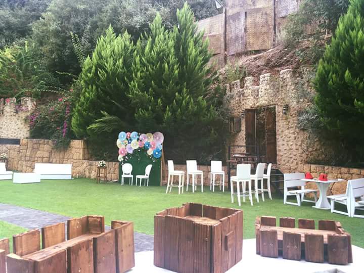 a lawn with chairs and tables and a wall with trees