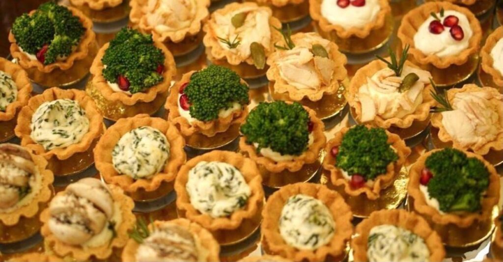 "Kaakat Gourmet presents a group of small tartlets with delicious food on them."