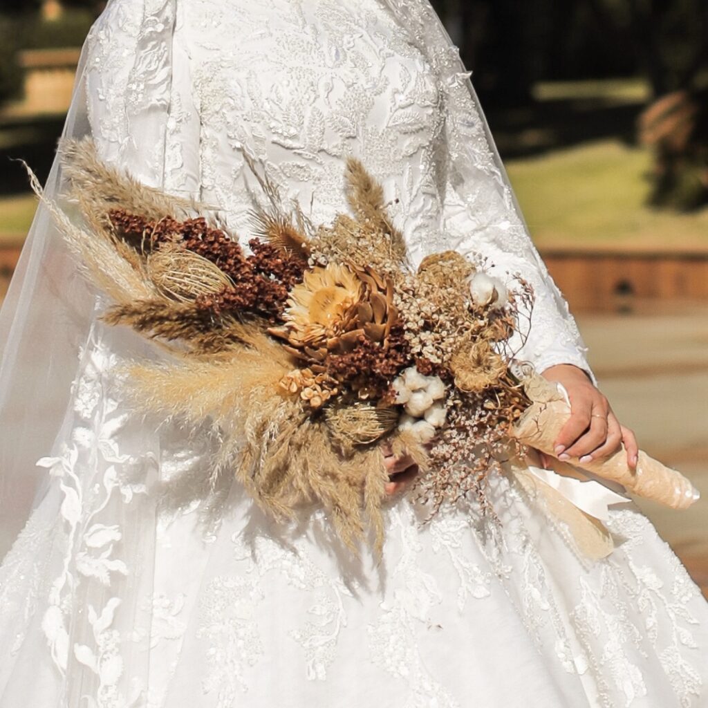 a woman in a wedding dress holding a bouquet of dried flowers