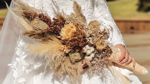 a woman in a wedding dress holding a bouquet of dried flowers