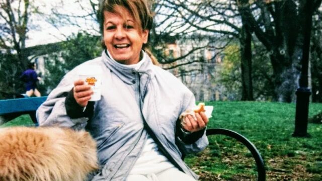 a woman sitting on a bench with a cat and a hot dog