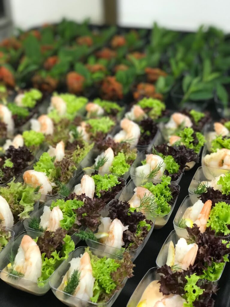 "A group of small plastic containers with shrimp and lettuce, provided by OSTRA Catering."