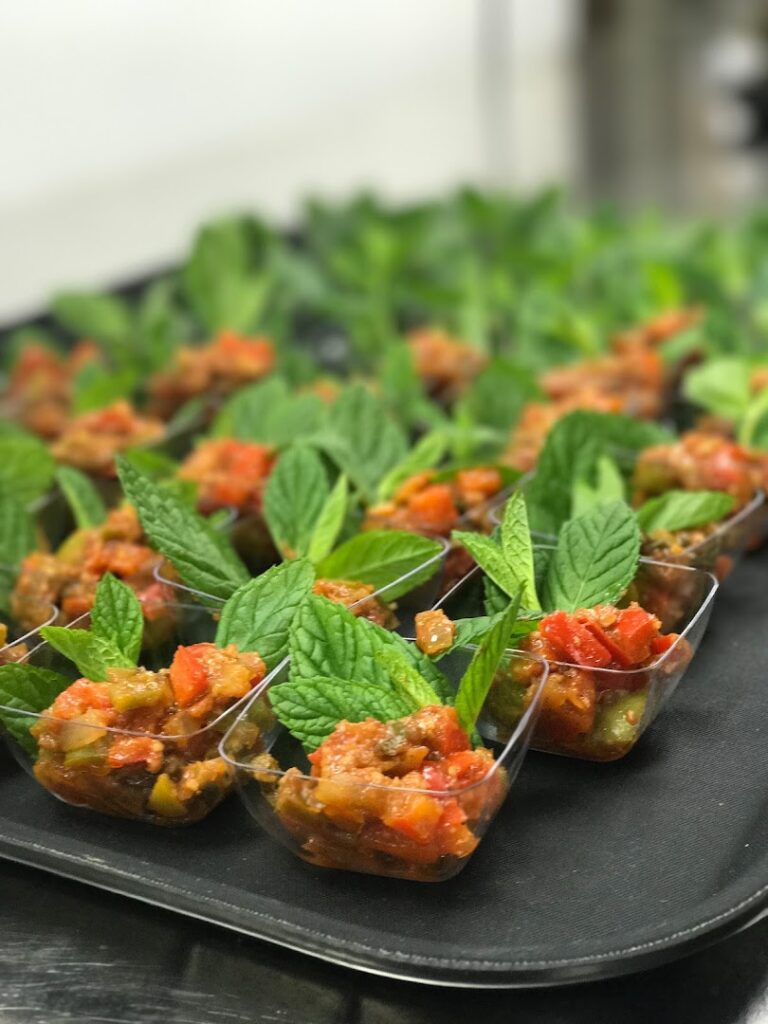 "A tray of small plastic cups with food in them, catered by Ostra Catering."