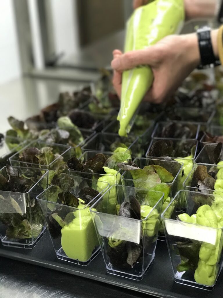 "A person from Ostra Catering pouring green sauce into small plastic cups."