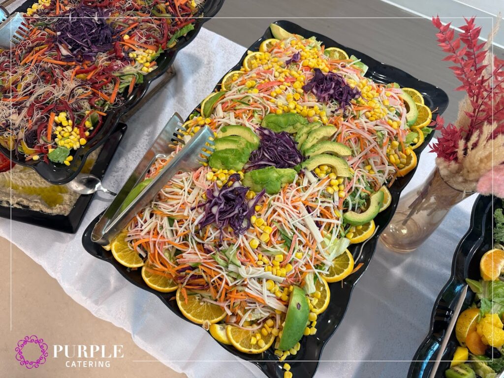 There is a trays of food on a table catered by Purple Catering & Events.
